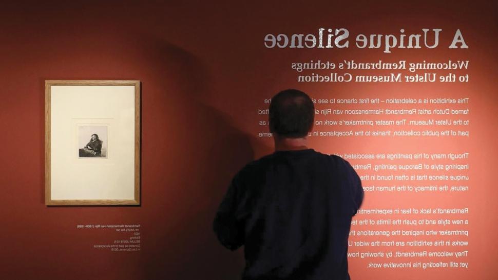 一名男子在读着写在一面橘黄色大墙上的“独特的沉默”展览的描述